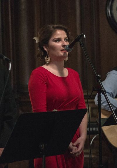 Tess Howell in a red dress singing into a microphone.